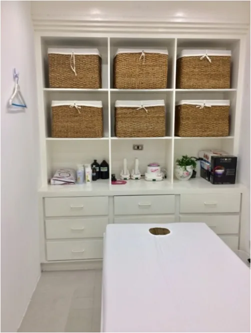 White treatment room with a massage bed and wicker baskets on the shelves