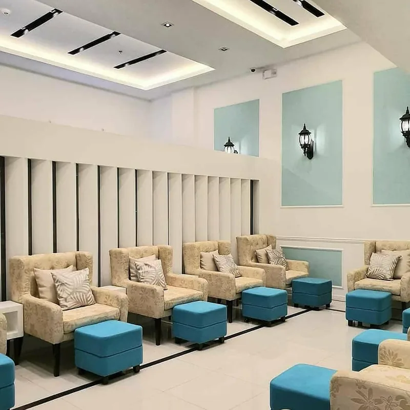 Pedicure lounge with cream wing chairs, teal footstools and pale-blue wall panels under lantern sconces